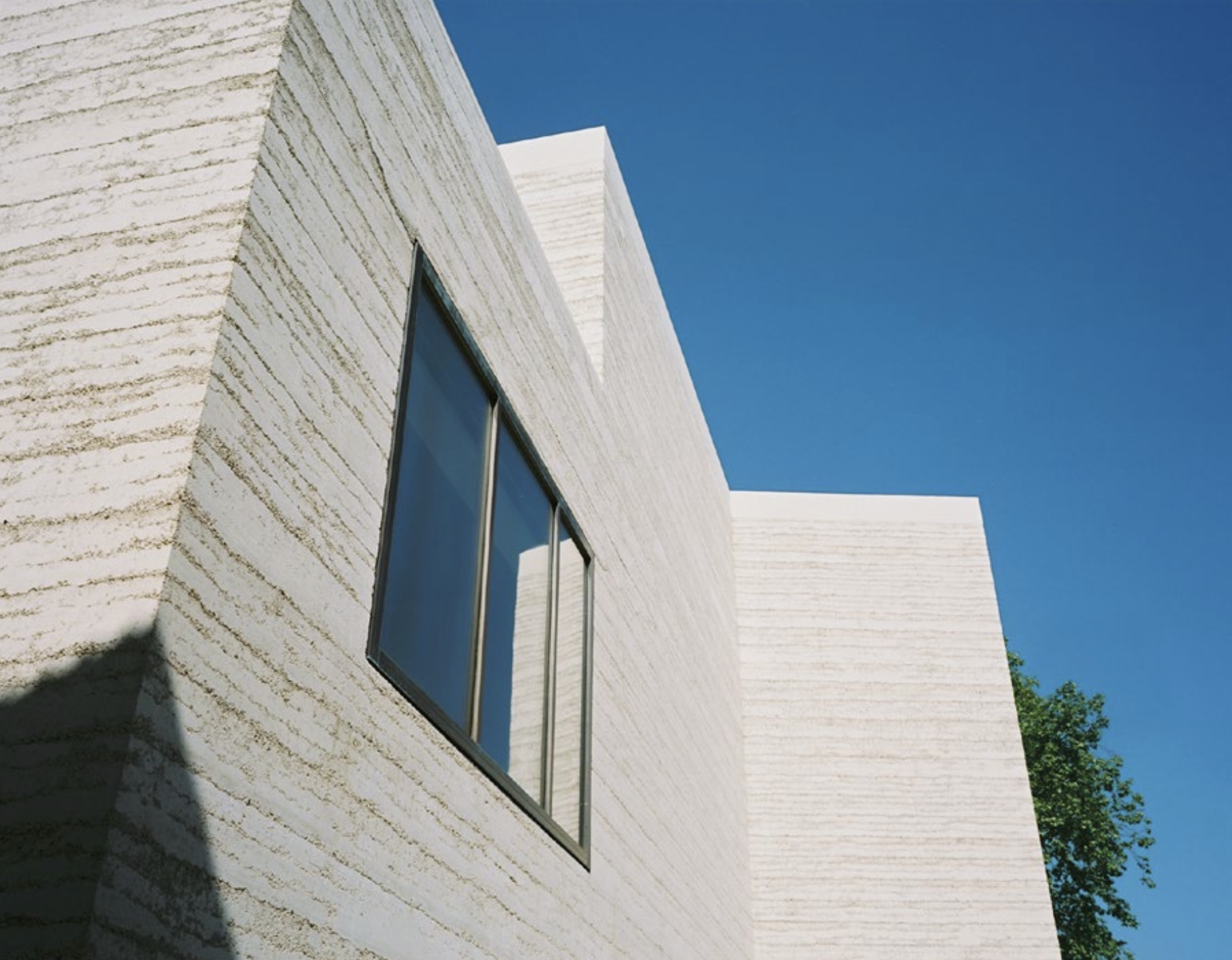Moderne Architektur mit strukturierten weißen Wänden und einem großen Fenster unter klarem blauen Himmel.